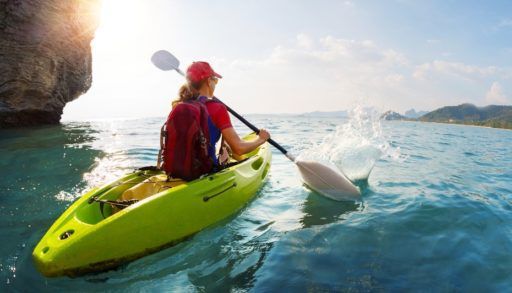 Woman in a red lifejacket and hat paddling a green kayak.