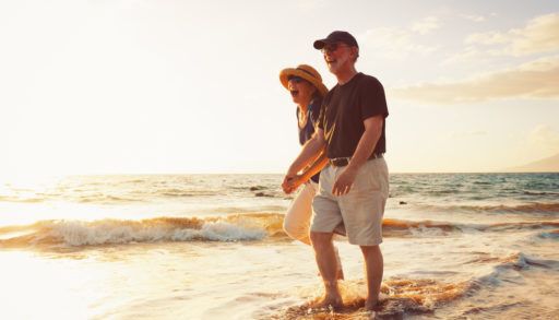 Smiling older couple walking hand-in-hand along a beach at sunset.