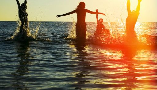 Silhouette of a group of friends jumping in an ocean at sunset.