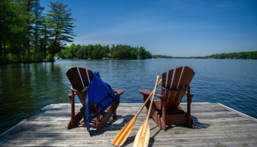 Two Adirondack chairs with canoe paddles on a dock looking out over a lake.