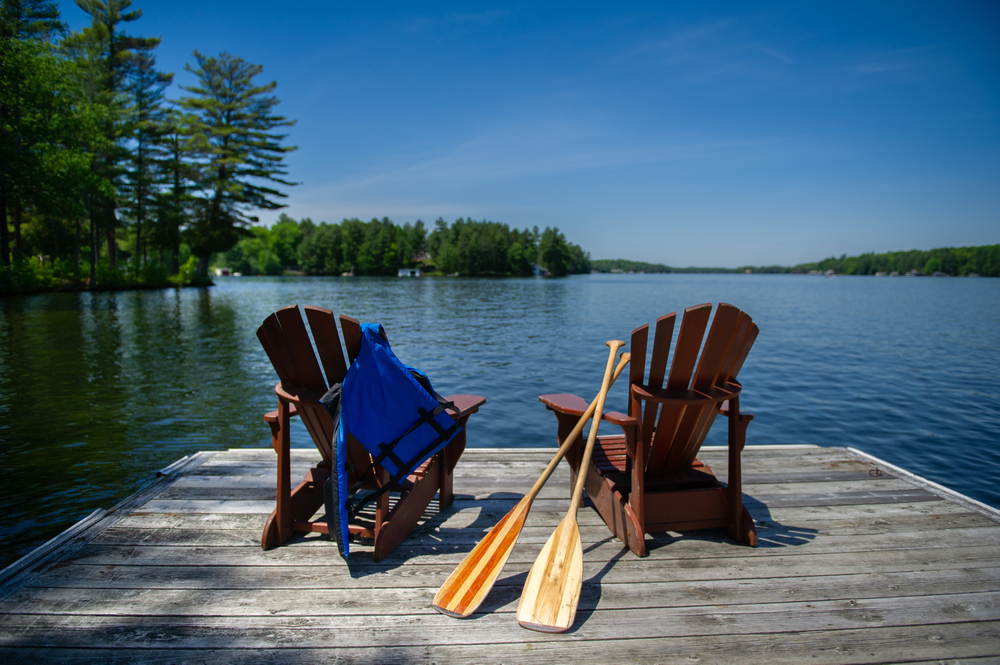 Two Adirondack chairs with canoe paddles on a dock looking out over a lake.