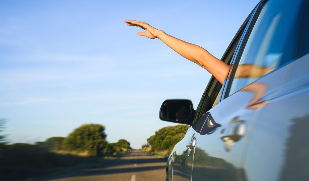 Person with their hand out a car window while driving.