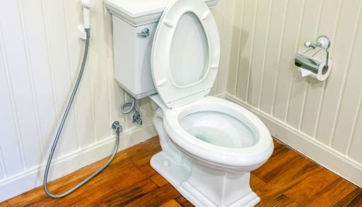A white toilet in a bathroom with white, wood panelling and dark wood floors.