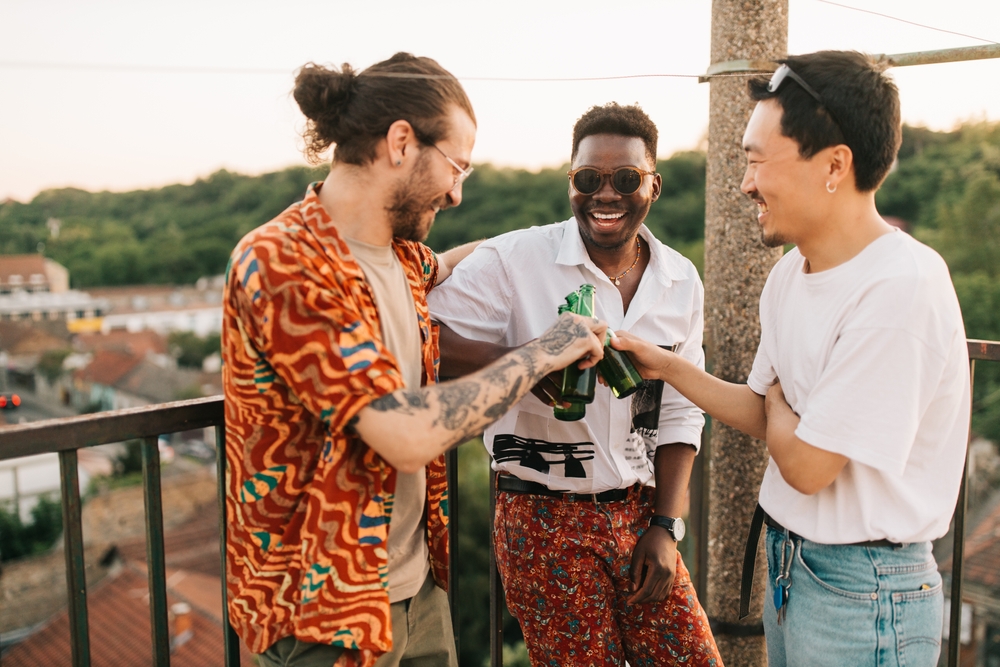 Three men toasting at a bachelor party on a rooftop balcony.