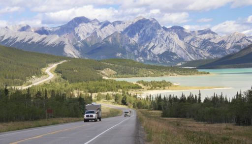 Truck pulling an RV on a road surrounded by mountains and near a lake on the Kootenay Plains, Alberta.