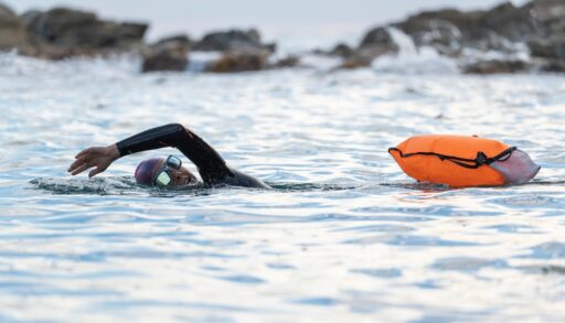 Woman swimming in open water with an orange buoy.