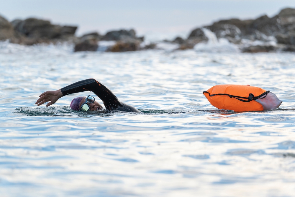 Woman swimming in open water with an orange buoy.