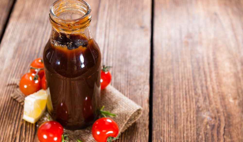 A bottle of barbecue sauce on a table next to small, red tomatoes.