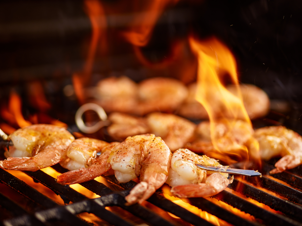 Close-up of shrimp on metal skewers cooking on a barbecue.