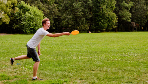 Young man throwing an orange frisbee in a green field.