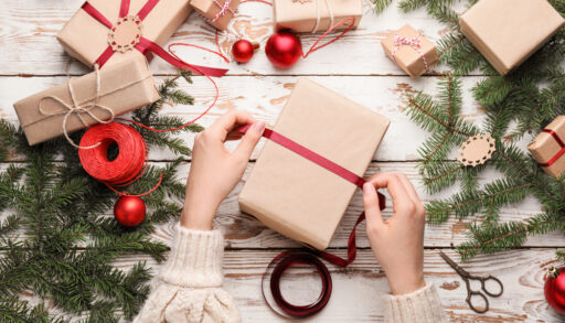 Overhead view of a woman's hands as she wraps a gift with brown paper and red ribbon.
