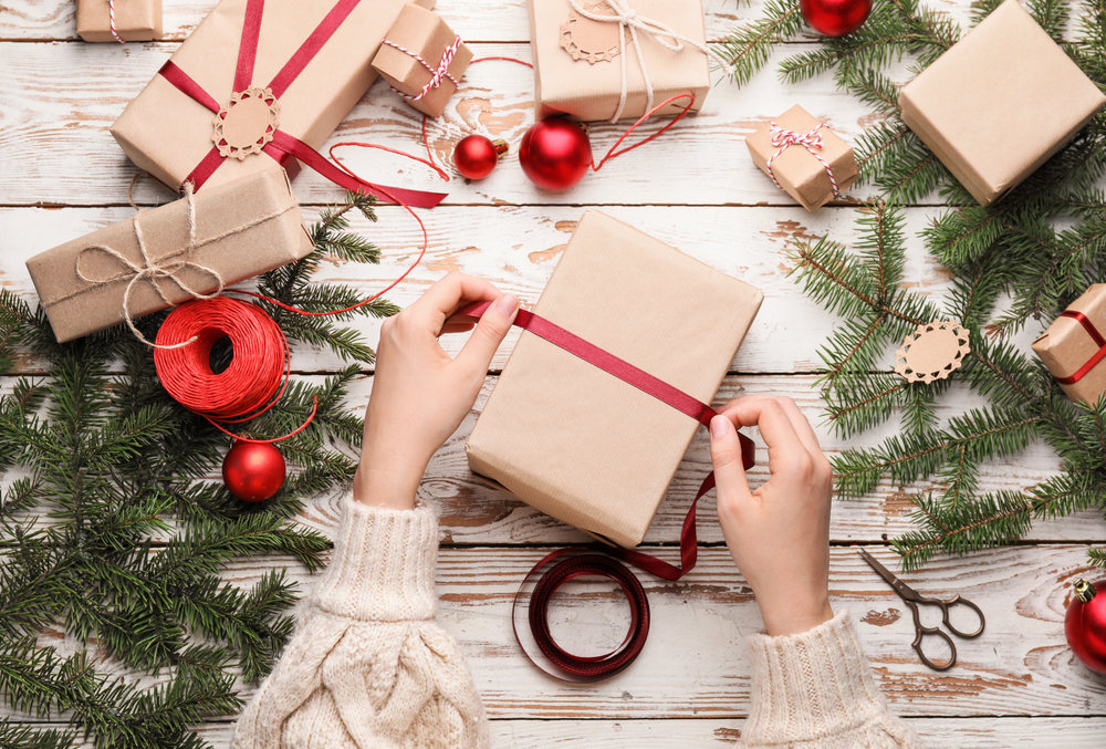 Overhead view of a woman's hands as she wraps a gift with brown paper and red ribbon.