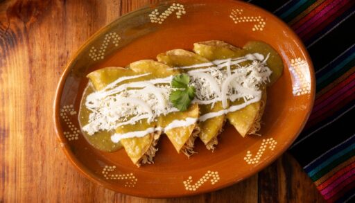 Overhead view of chicken enchiladas with a white sauce on a red plate.