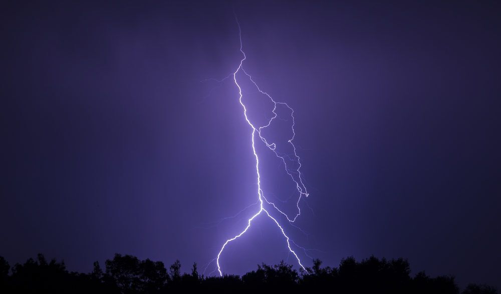 Lightning strike illuminates the silhouettes of trees.