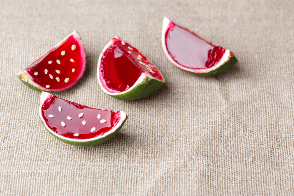 Close-up of watermelon jello shots made with lime rinds on a linen tablecloth.