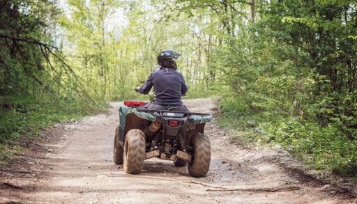 A man on an ATV driving on a dirt road in the middle of a forest.