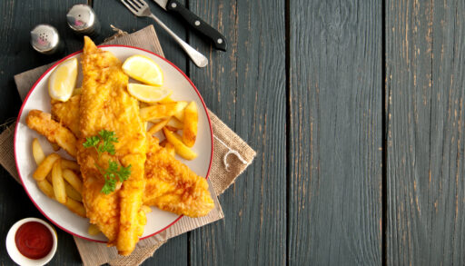 Overhead view of two pieces of fried fish on a plate next to a fork and knife.