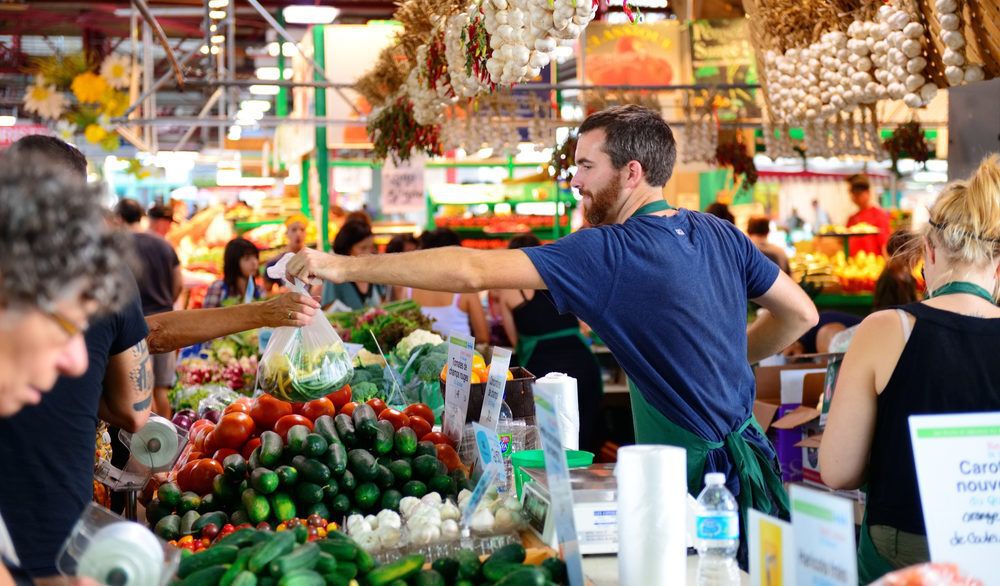 Man handing a bag of produce to a customer at a farmers' market.