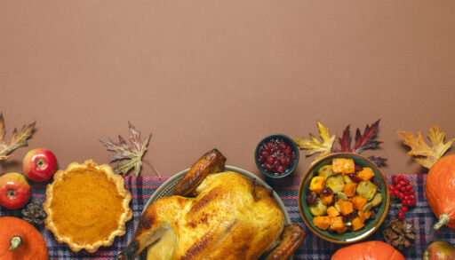 Flatlay image of a Thanksgiving table with a turkey, pumpkin pie, vegetables, cranberry sauce and pumpkins.