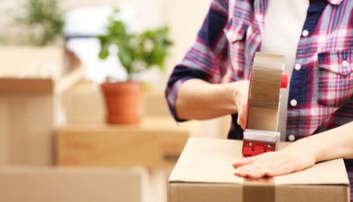 Close-up of a person in a plaid shirt packing boxes and taping them shut.