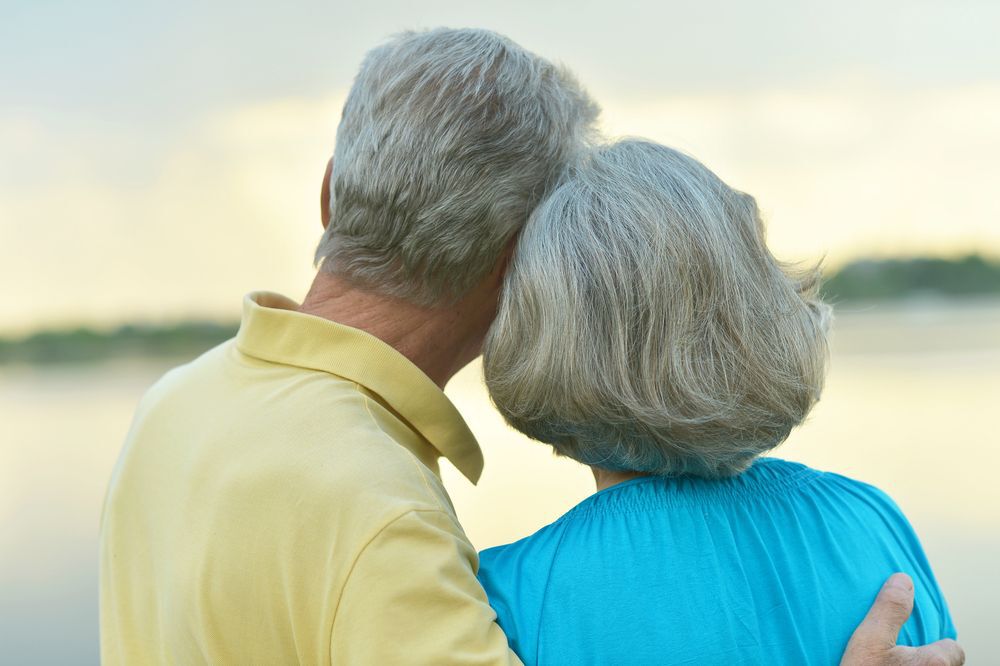 Retired couple standing looking at a lake.