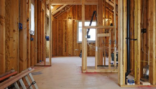 Home interior stripped down to its studs during construction, with exposed wires and a ladder on the floor.