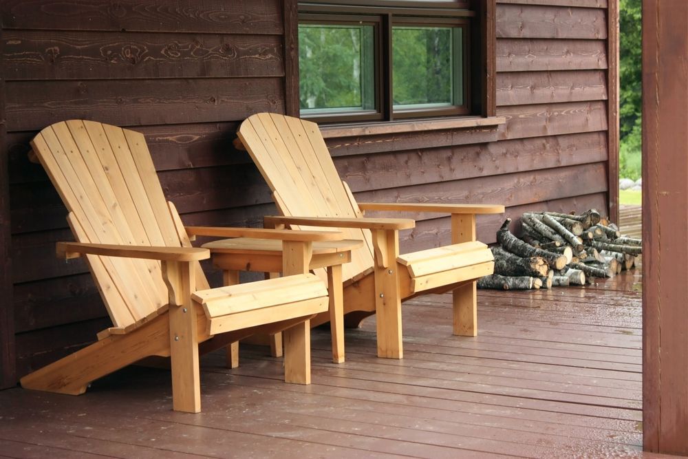 Dark brown porch with two light-coloured Muskoka chairs covered in rain drops.