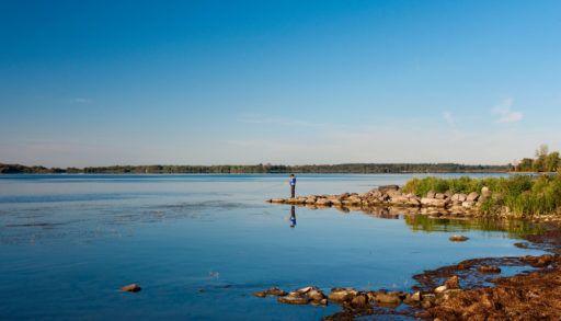 A kid standing on rocks, fishing in the St. Lawrence River.