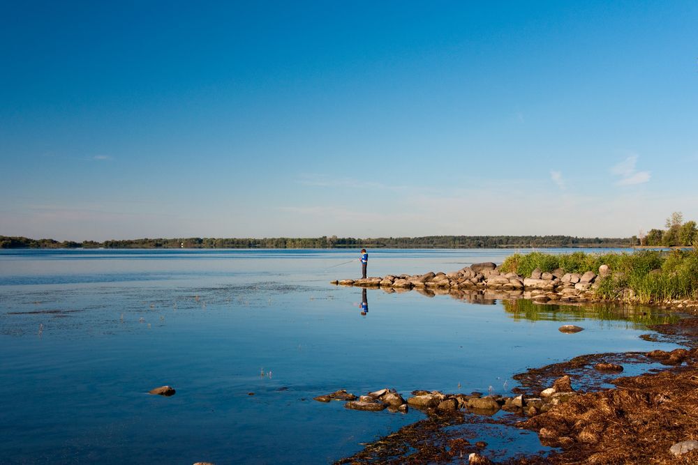 A kid standing on rocks, fishing in the St. Lawrence River.