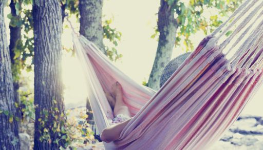 A person sleeping in a hammock next to a lake.