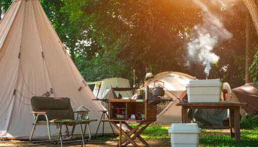 A white tent surrounded by camping equipment, including a chair, stove and table.