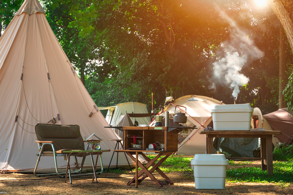 A white tent surrounded by camping equipment, including a chair, stove and table.