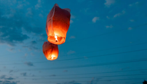 Two red paper lanterns floating in the sky at dusk.