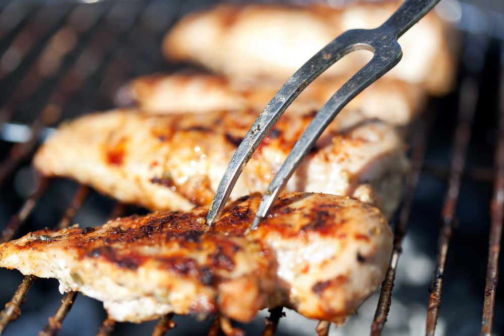 A two-pronged fork stabbing a grilled chicken breast.