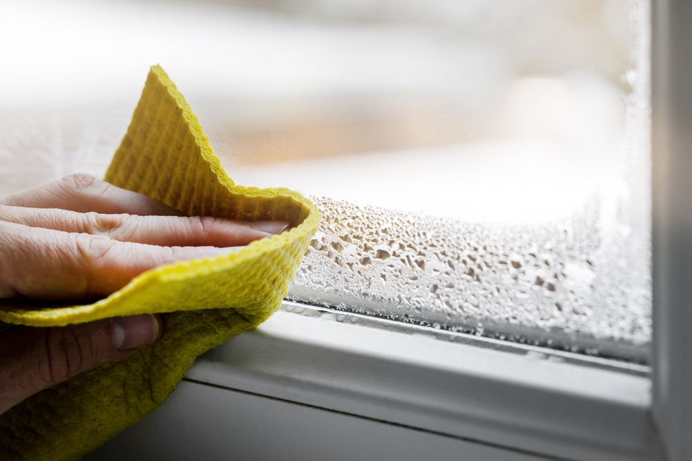 Close-up of a person's hand holding a yellow cloth as they wipe condensation from a window.