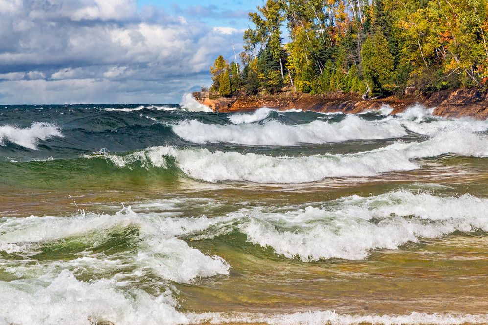 Blue and green waves crashing on the shores of Lake Superior with a green forest surrounding the water.