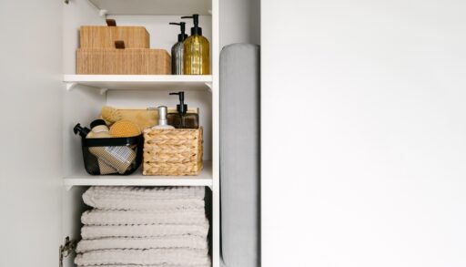 A bathroom closet with folded grey towels and wicker baskets for storage.