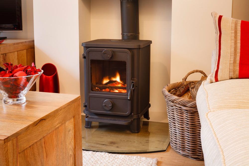 A black wood stove in a living room next to a sofa and a basket for firewood.