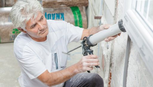An older man calking a wall.