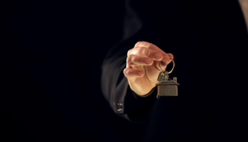 Close-up of a man's hand holding a keychain with a house on it.