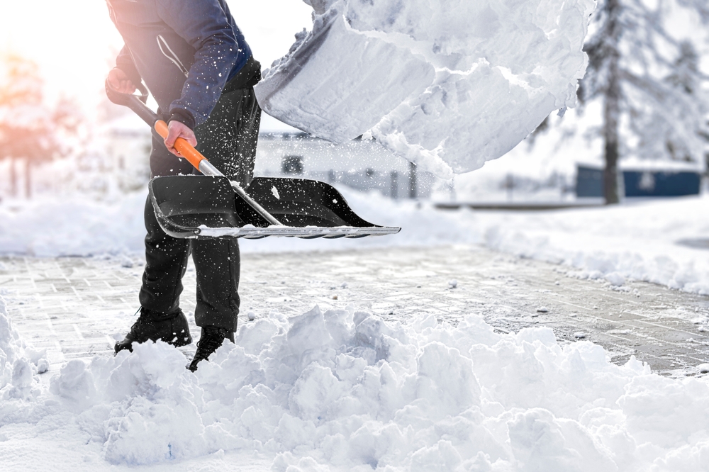 Close-up of snow flying in the air as a man shovels his driveway.