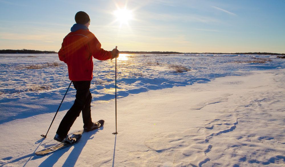 A man in a red coat cross-country skiing with the sun shining in the background.