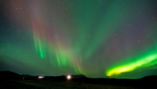 Green and purple Northern Lights over a silhouetted landscape.