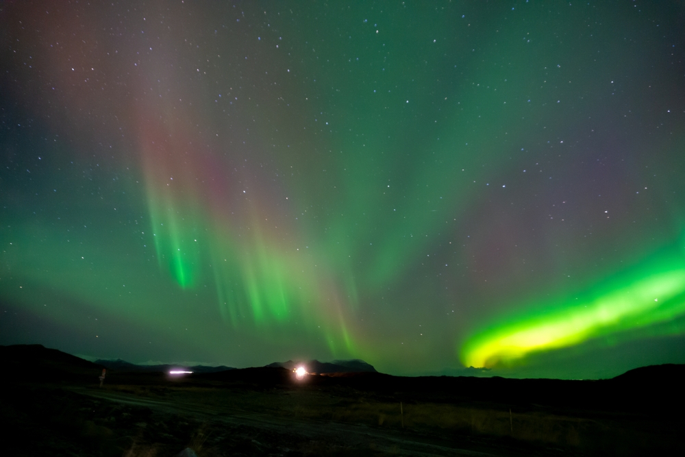 Green and purple Northern Lights over a silhouetted landscape.