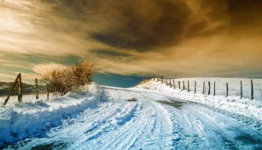 A snow-covered country road with a yellow sky at sunset.