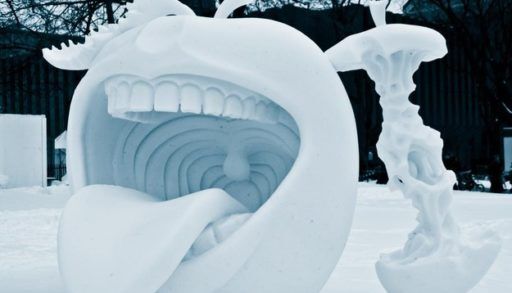A snow sculpture of an apple with a mouth next to an apple core