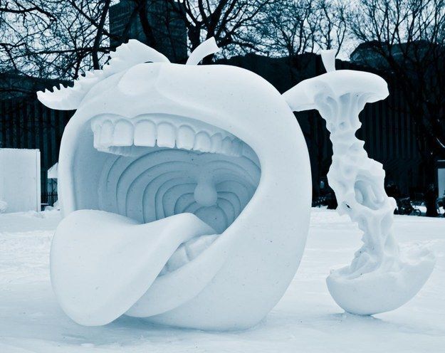 A snow sculpture of an apple with a mouth next to an apple core