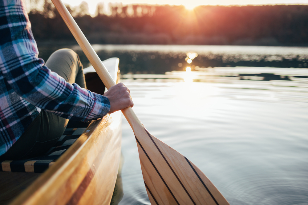 Person rowing a canoe in a calm lake at sunset.