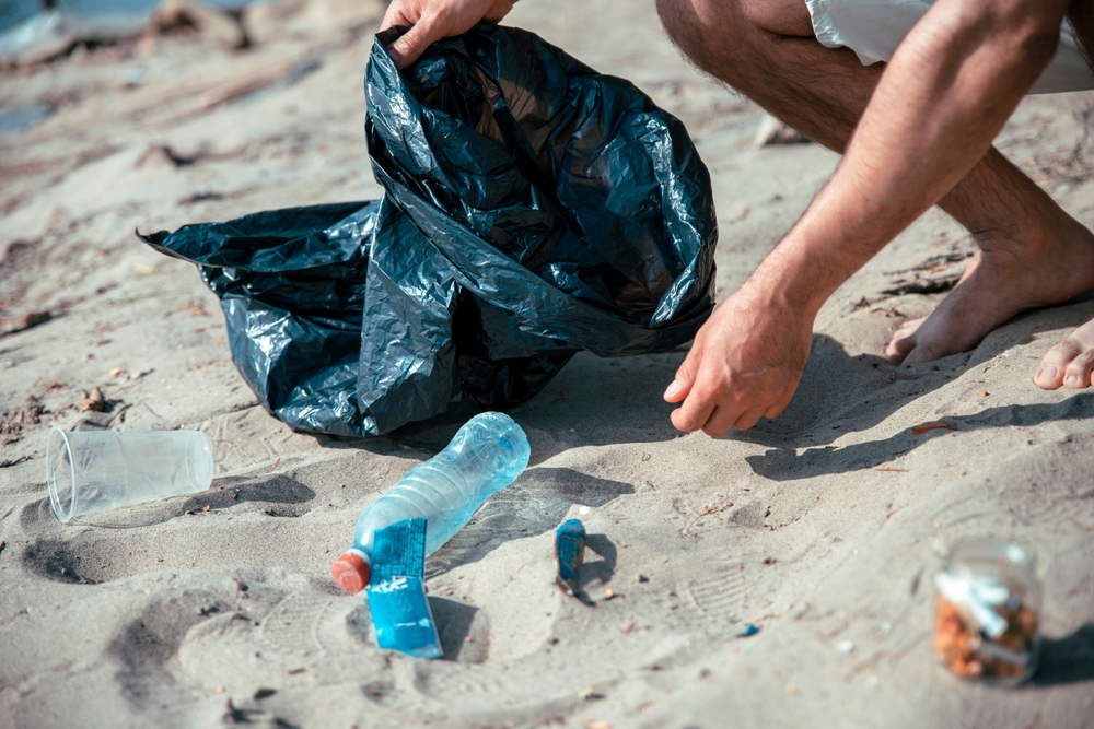 Person picking up trash on a beach.