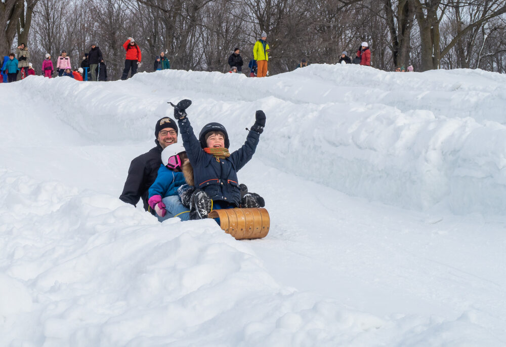 Family having fun sledding down a snowy hill.